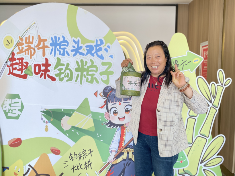 2025年5月30日，石龙湖服务区开展“趣味钩粽子”活动，旅客手拿礼品在活动海报前打卡留念。（拍摄者：董静）.png